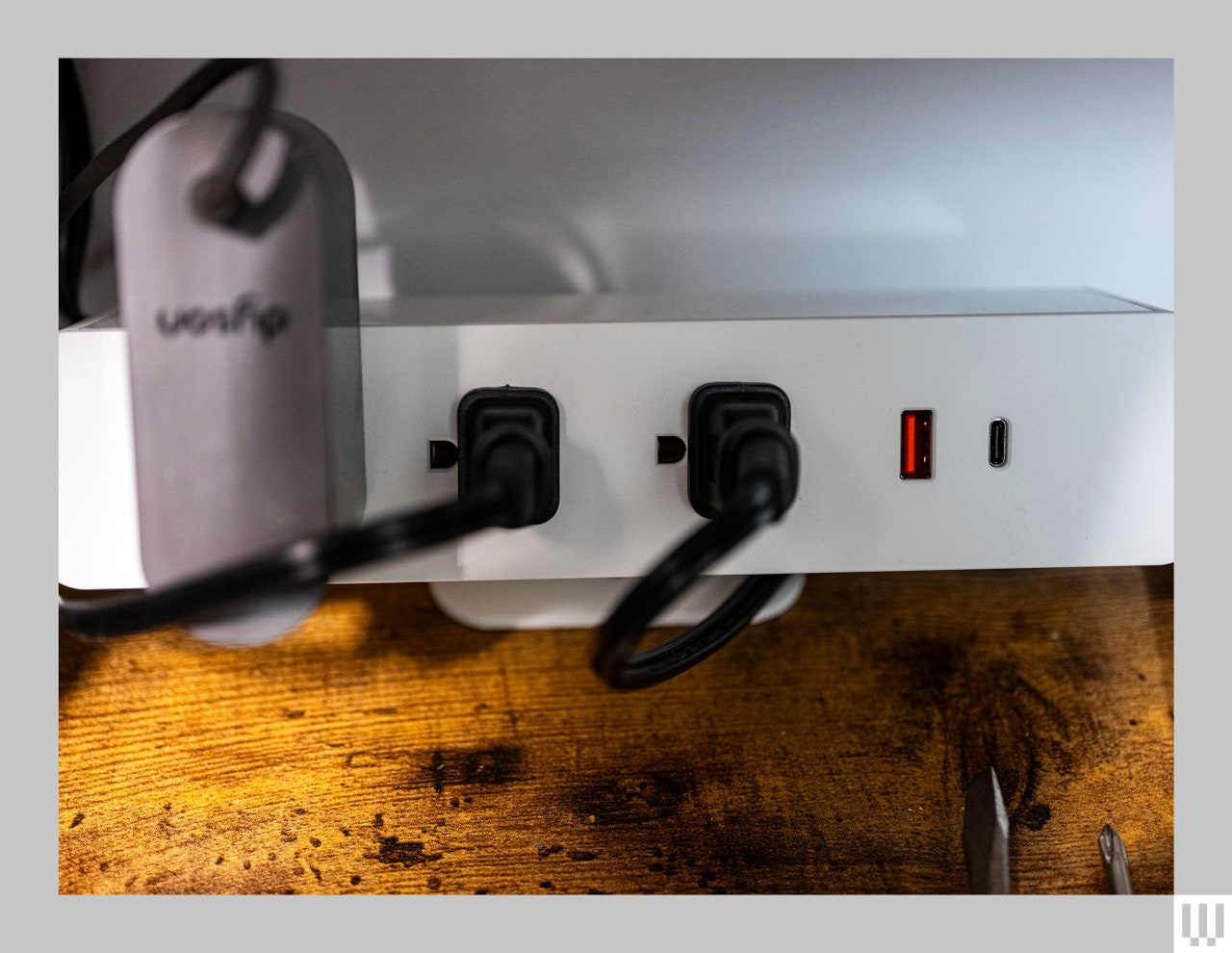 Front view of Branch Clamp On, a white electrical power strip gripping the edge of a wooden desk