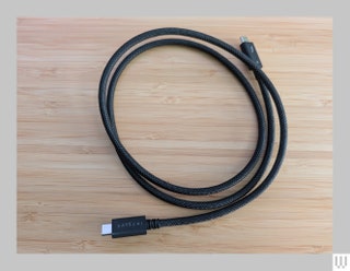 Satechi Thunderbolt 4 Pro Cable in black wrapped up in a circle sitting on a wooden surface