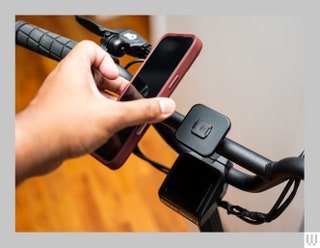 Peak Design Universal Bar Mount clipped onto the handlebars of a bike with a hand about to snap a mobile phone to it