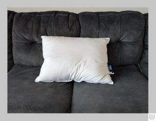 Front view of the Brooklinen Down Pillow a fluffy white pillow on a dark grey couch