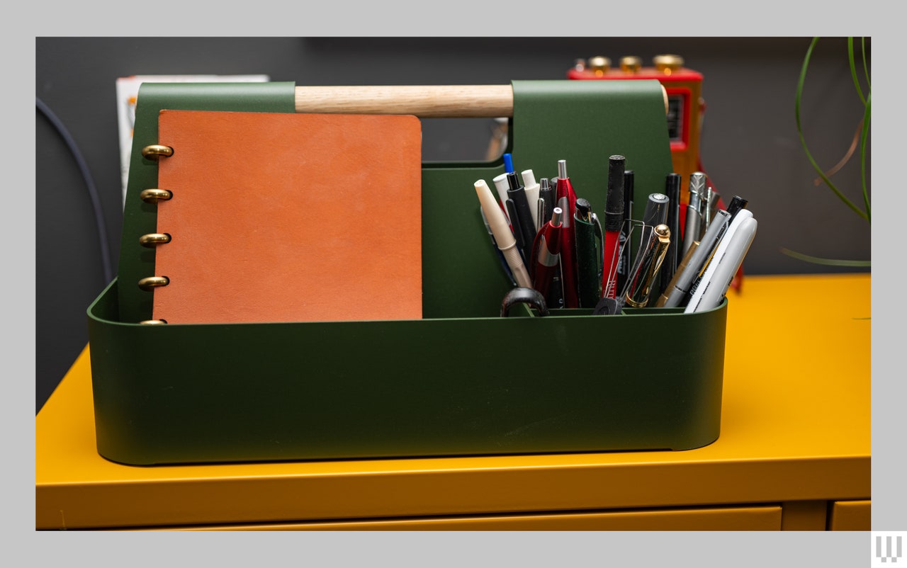 Branch Most Modest Desk Caddy in dark green, a rectangular container with components and a wooden handle, sitting on a yellow metal locker