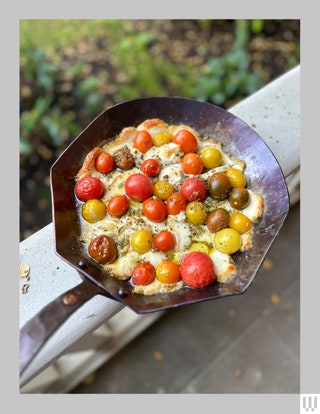 Copper State Forge 10Inch Hybrid Carbon Steel Skillet on the top of a metal handrail with tomatoes and veggies cooked...