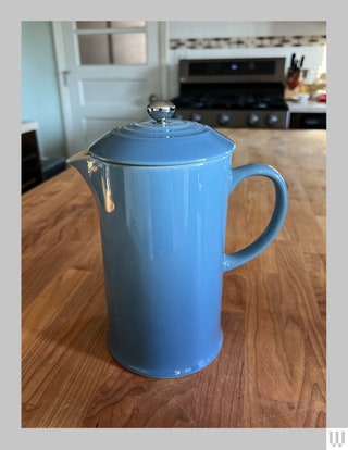 Le Creuset French Press in blue sitting on a wooden countertop