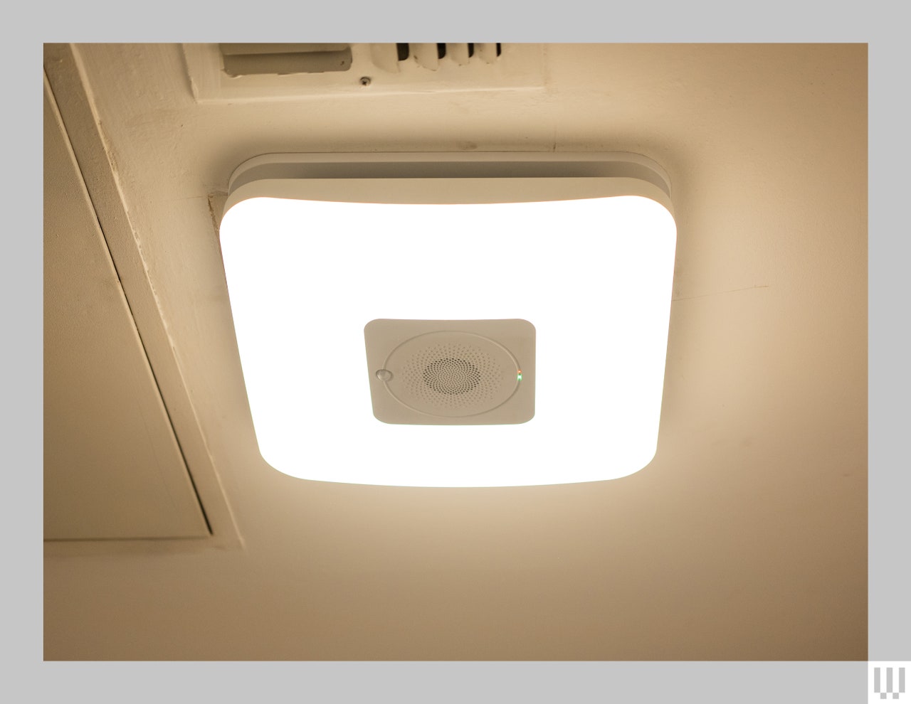 View looking upward toward the ceiling at an installed Commercial Electric Smart Bathroom Exhaust Fan, emitting white light around the center vent