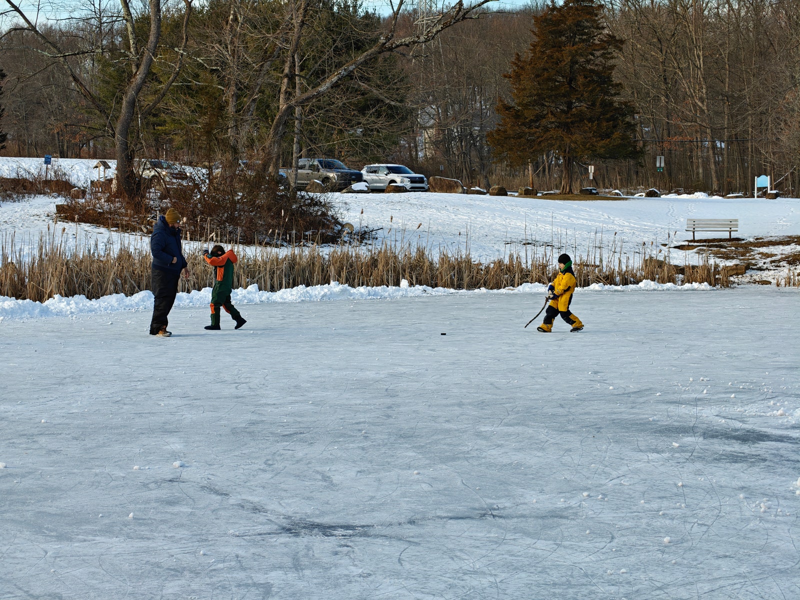 A photo taken with OnePlus 13 using 3x optical zoom showing two kids and an adult playing on a snowcovered frozen lake