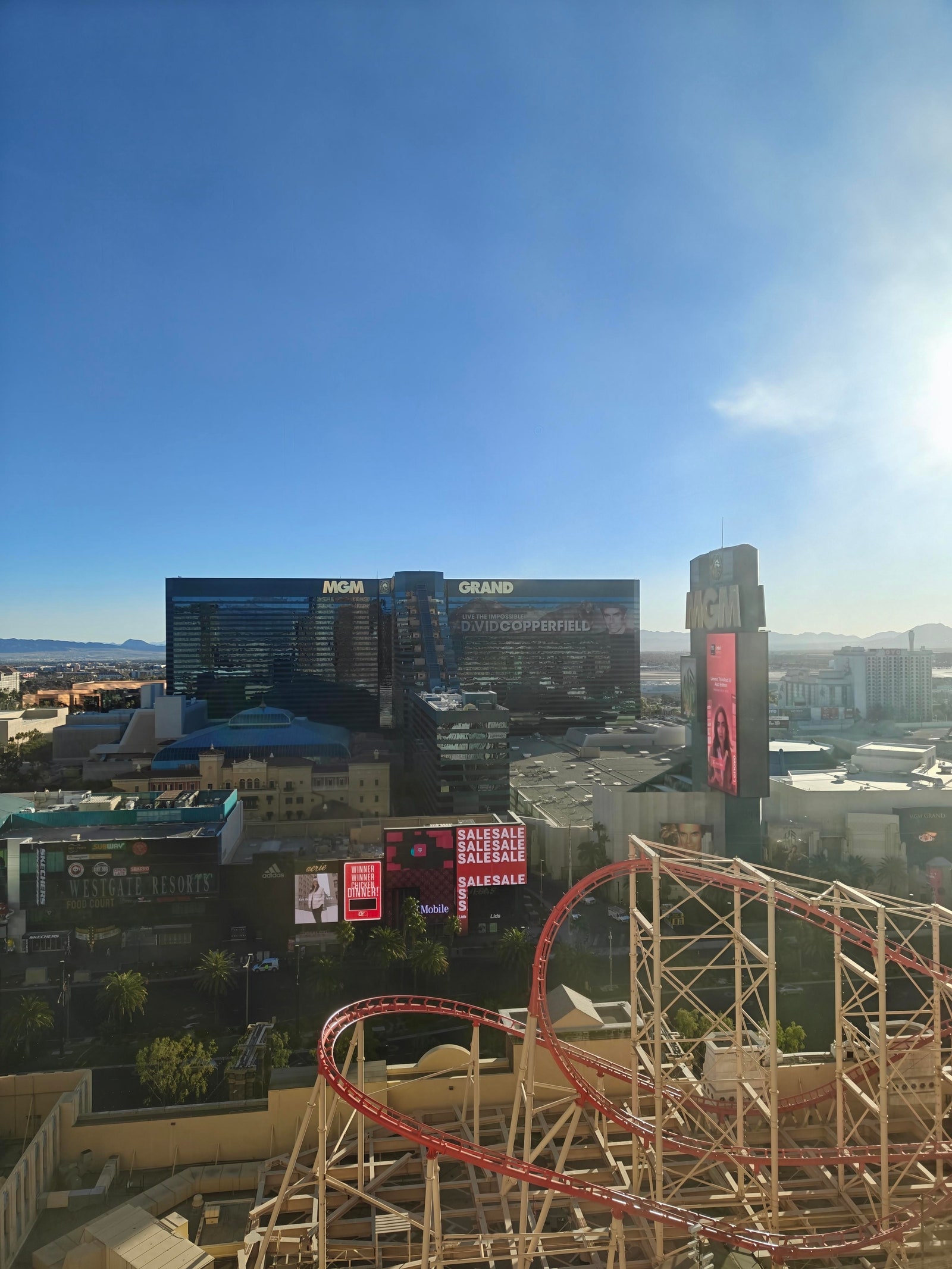 A photo taken with the OnePlus 13R through the glass of a window showing large glass buildings and a rollercoaster on a...