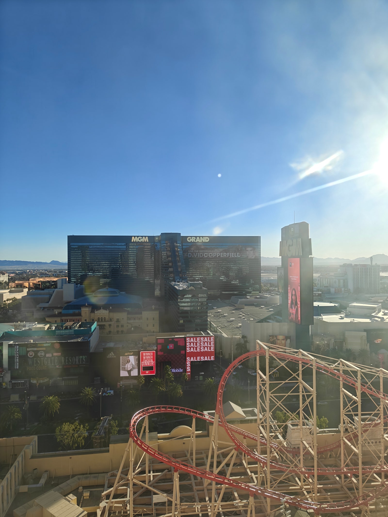 A photo taken with the OnePlus 13R through the glass of a window showing large glass buildings and a rollercoaster on a...