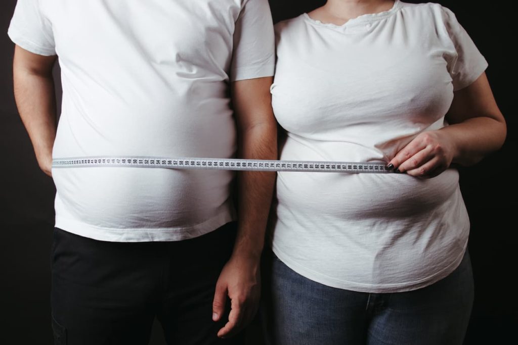 Overweight couple standing together wrapped with measure tape.