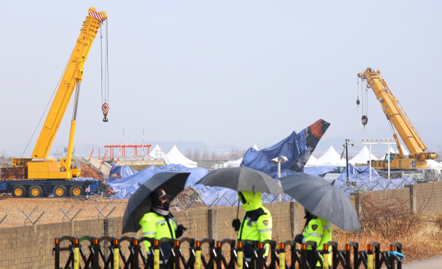 5일 오전 우산을 쓰고 근무하는 경찰관들 뒤로 전남 무안국제공항 사고현장 및 꼬리 날개에 방수포가 덮여 있다. 연합뉴스