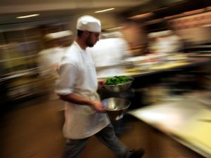 A culinary student rushes through the kitchen with greens during a class for aspiring professional chefs.