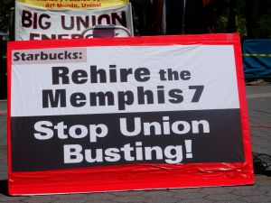 A sign reads "Rehire the Memphis 7 Stop Union Busting" in black letters on a red and white banner.