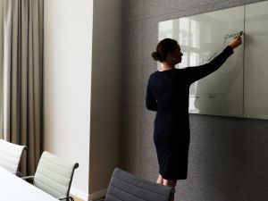 A woman stands at a whiteboard in a conference room and draws a curve diagram.