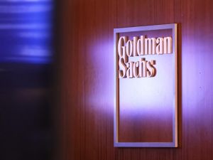The Goldman Sachs logo is pictured on a brown wooden wall.