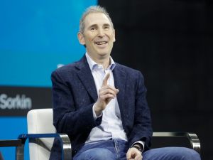 Close-up of Andy Jassy, raising a finger, while dressed in a navy blue blazer and blue jeans.