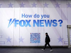 A person walks past the Fox News Headquarters at the News Corporation building. A sign reads, "How do you Fox News?"