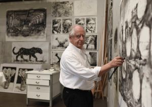 A man stands surrounded by drawings in a studio