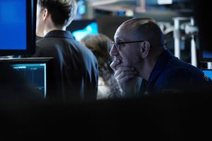 A worried man looks at a computer screen, holding his head in his hands.