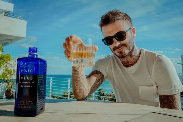 Beckham holding whiskey with the bottle next to him.