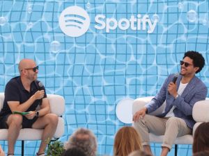 Daniel Ek sits beside Trevor Noah in front of a sign with a Spotify logo.