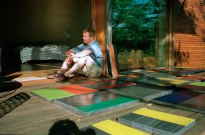 A man sits on a patio with several abstract coloblock paintings