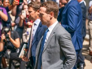 A side profile of Mark Zuckerberg whith a large crowd of photographers in the background.