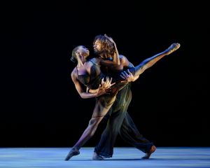 A male dancer holds a female dancer with her splayed legs stretched