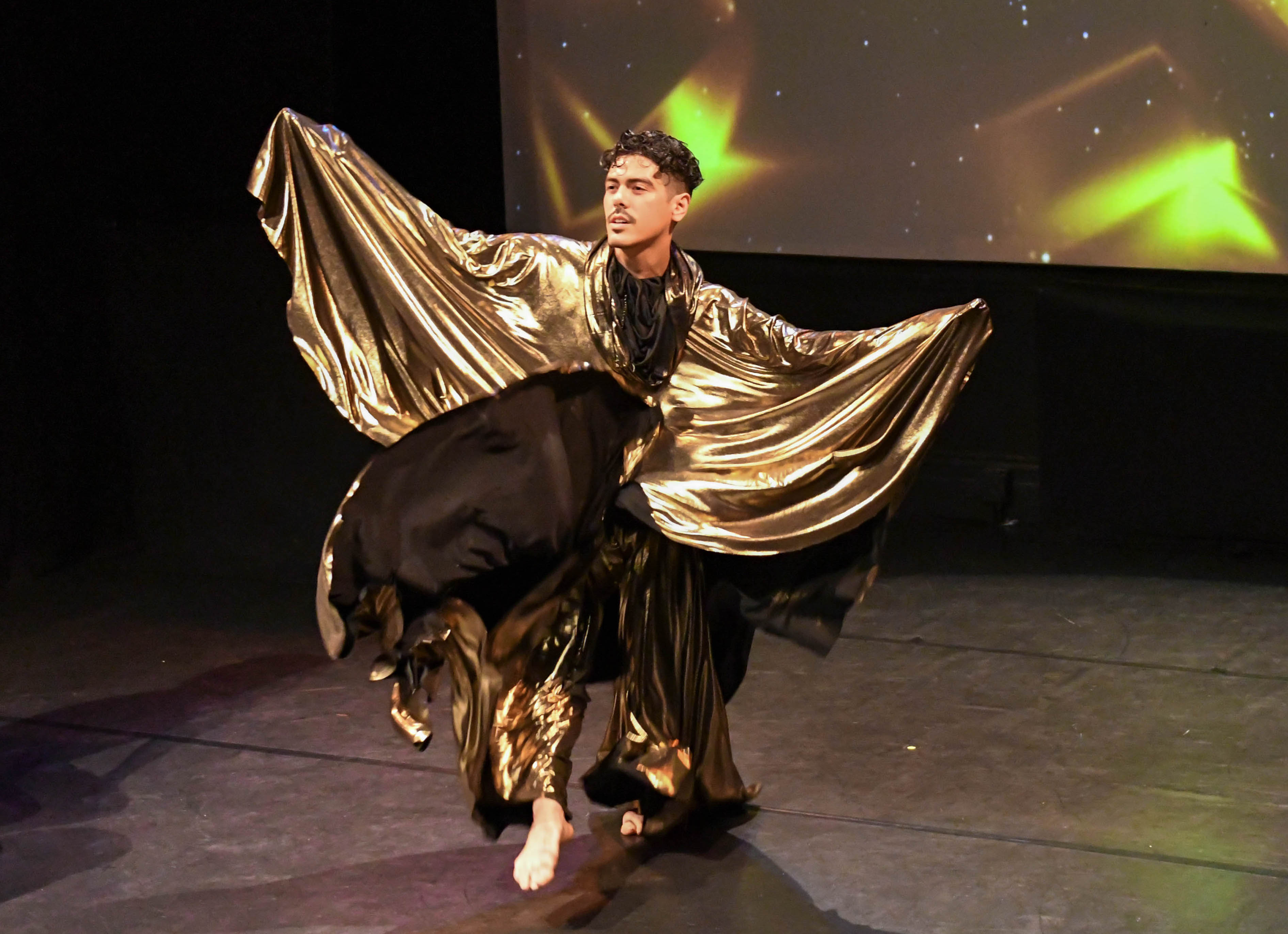 A dancer wearing a voluminous golden costume spreads their arms wide