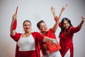 Three women in various outfits of red and white pose energetically with props
