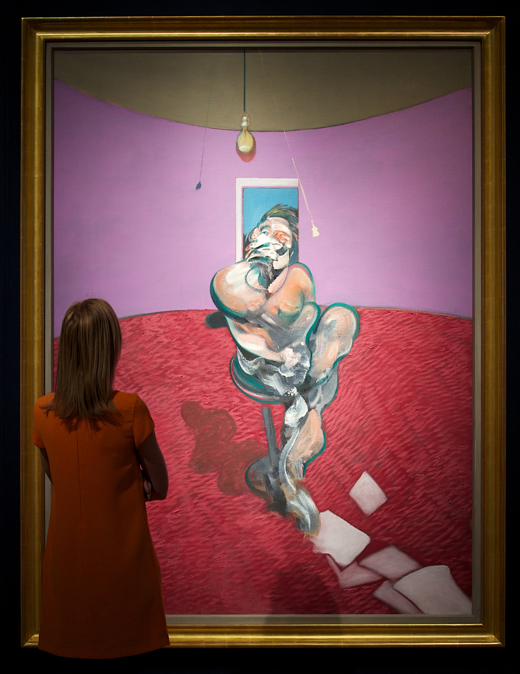 Woman looks at pink and purple painting of male figure