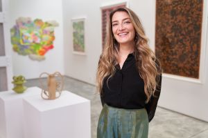 A woman wearing a black top stands in an art gallery filled with colorful works