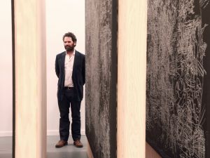 Man in suit stands in between paintings