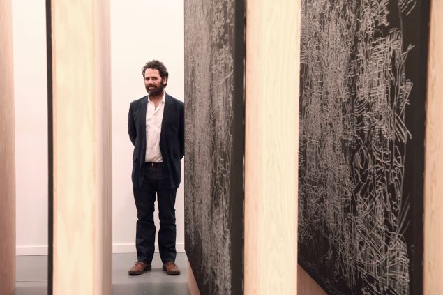 Man in suit stands in between paintings
