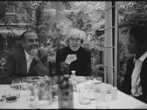 Black and white photo of three people sat at outdoor table