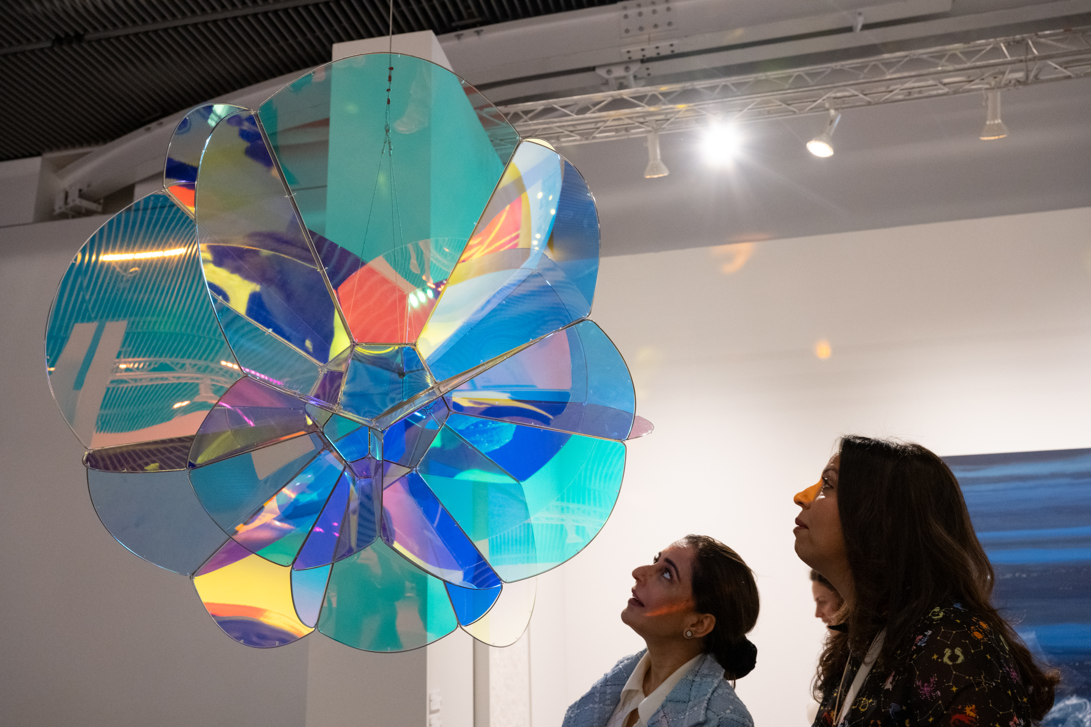 Art fair goers look at a colorful hanging sculpture of shimmering multicolor plexiglass 
