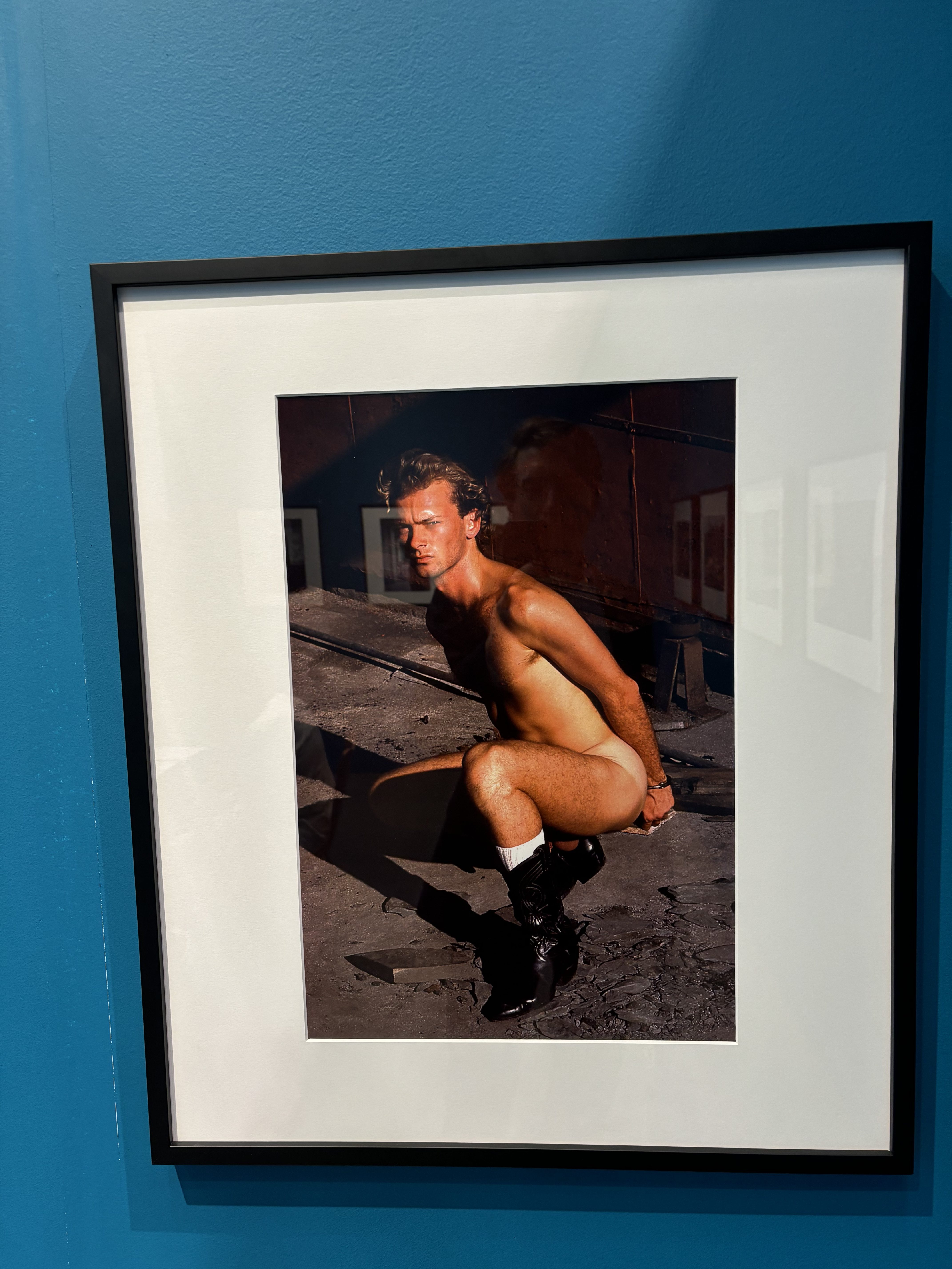 A nude photo of a man in a frame hanging on a blue wall
