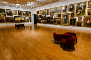 The interior of a roomy art museum with gilt frame paintings on the walls