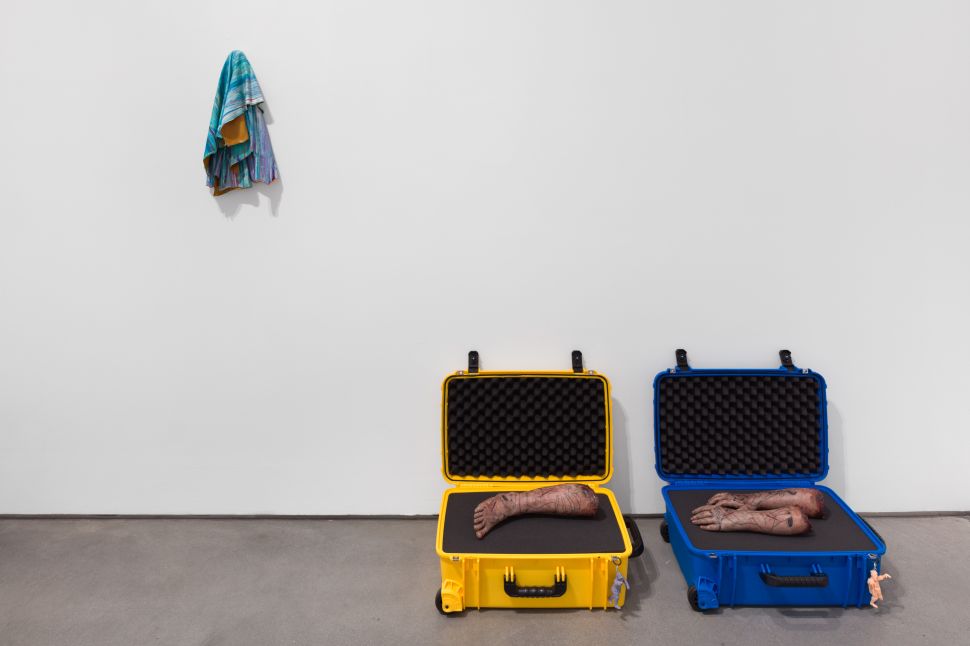 Installation view with two sculptural works, one textile hanging from the wall, and two suitcases with body parts.