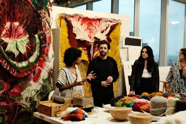 Three people stand in discussion near displays of fiber art