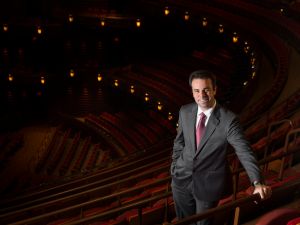 Man in suit stands in front of rows of empty opera seats