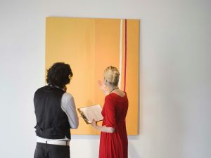 Two people stand in front of a large orange painting