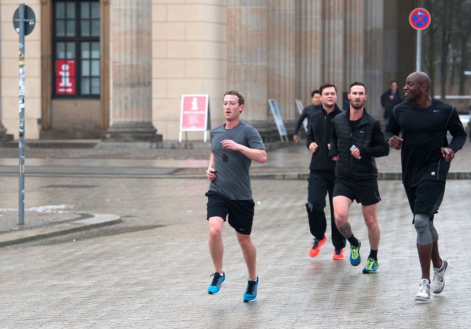 Man in grey shirt runs down street, with men in black shirts following closely behind