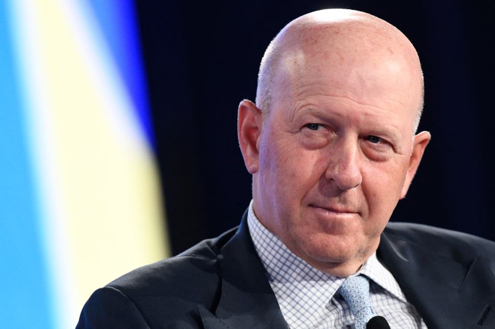 Man in suit, white shirt and blue tie sits onstage during panel