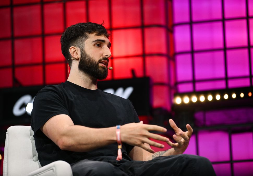 Man in black t-shirt sits in chair onstage in front of pink and red screen 