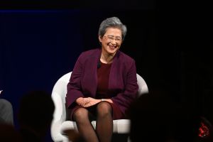 Woman in burgundy blazer suits in white chair onstage