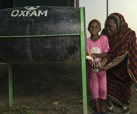 Woman and child washing their hands at Oxfam supported water tank.