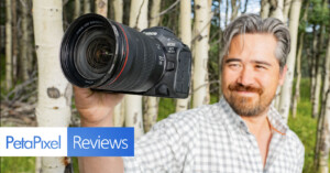 A person with gray hair and a beard holds up a Canon EOS R5 camera against a background of trees. The photo includes a "PetaPixel Reviews" logo in the bottom left corner.