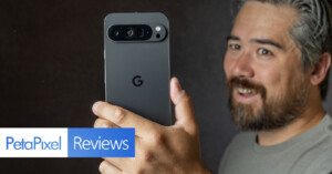 A person holds up a Google Pixel smartphone facing the camera. The phone's camera array is visible. The person has a beard, mustache, and gray hair. "PetaPixel Reviews" is prominently displayed in text on the left side of the image.