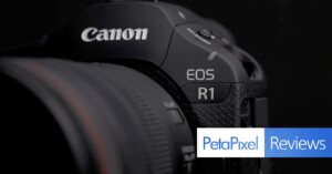 Close-up of a Canon EOS R1 camera showing part of the lens, brand name, and model. Petapixel Reviews logo is partially visible in the lower right corner against a dark background.