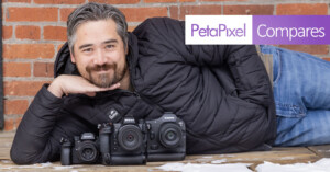 A person lying on a wooden deck poses with three cameras from Sony, Nikon, and Canon. The person is smiling, resting their chin on their hands. A brick wall serves as the background. The text "PetaPixel Compares" is displayed in the top right corner.