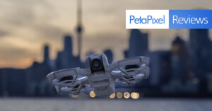 A drone hovers in the foreground with a blurred city skyline and sunset in the background. The image features a "PetaPixel Reviews" banner in the top right corner.